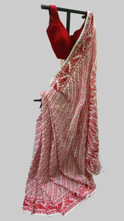 A red and white patterned saree draped on a black hanger with a red sleeveless blouse, set against a cream-colored fabric backdrop.