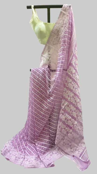 A lavender and white patterned saree draped on a black hanger with a light green blouse, set against a beige fabric backdrop.