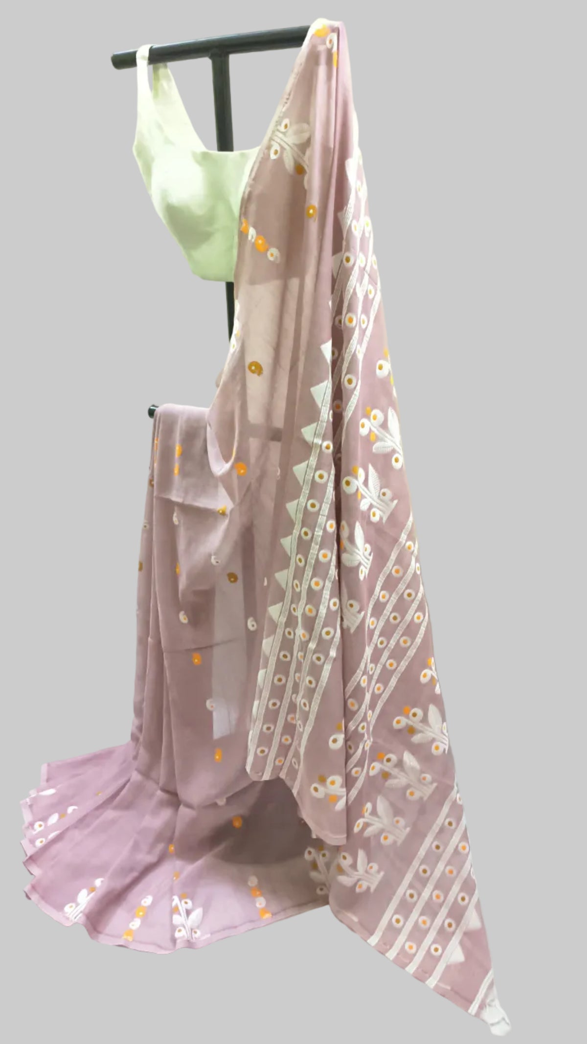 A dusty pink traditional saree draped on a black clothing rack, featuring white floral patterns and yellow-gold mirror work along the border, paired with a light green blouse.
