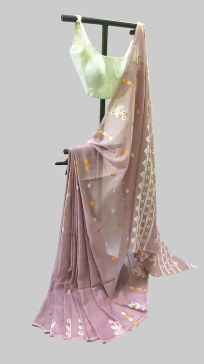 A mauve pink saree with white and orange floral patterns and a white geometric border, paired with a light green sleeveless blouse, displayed on a black clothing stand against a draped white fabric backdrop.