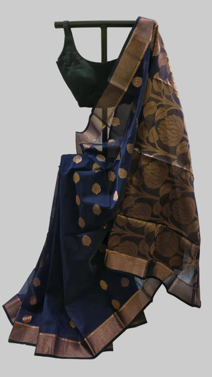 A navy blue silk saree with gold zari floral motifs and borders, paired with a black sleeveless blouse, displayed on a black hanger against a beige fabric backdrop.
