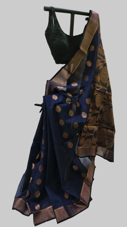A navy blue silk saree with metallic bronze-gold zari motifs and border, paired with a black blouse, displayed on a black clothing hanger against a draped off-white fabric backdrop.