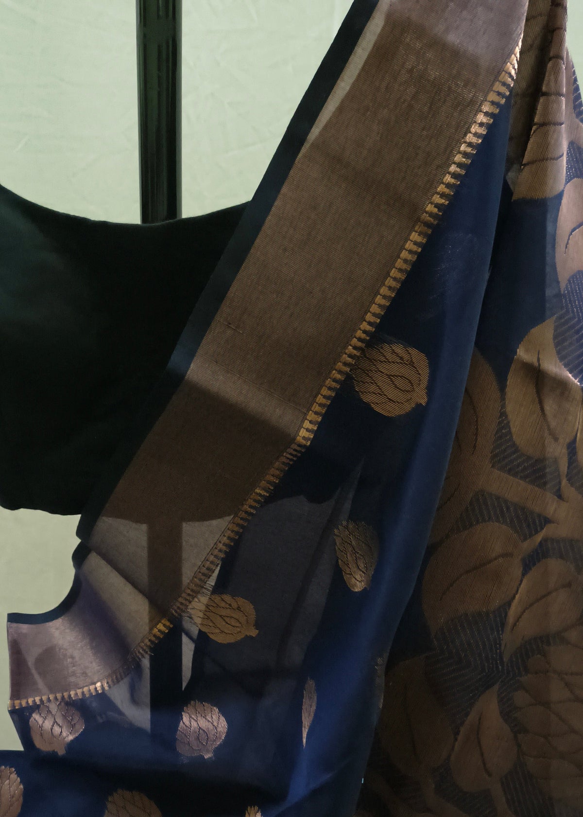 A close-up of a dark blue Banarasi silk saree with metallic gold floral motifs and a wide gold border, paired with a black blouse.