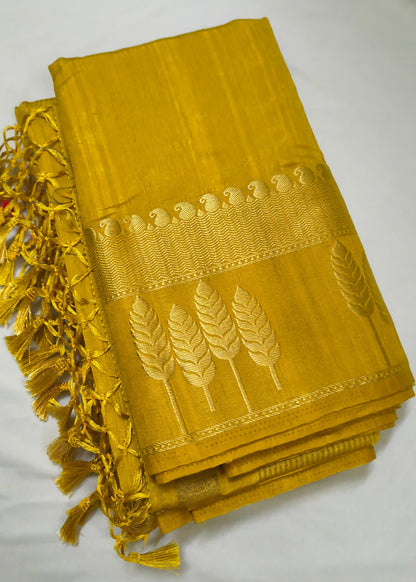 A folded mustard yellow silk saree or fabric piece with gold zari embroidery depicting wheat stalks and a decorative border, finished with a matching yellow tassel fringe on the left side, displayed on a white fabric background.