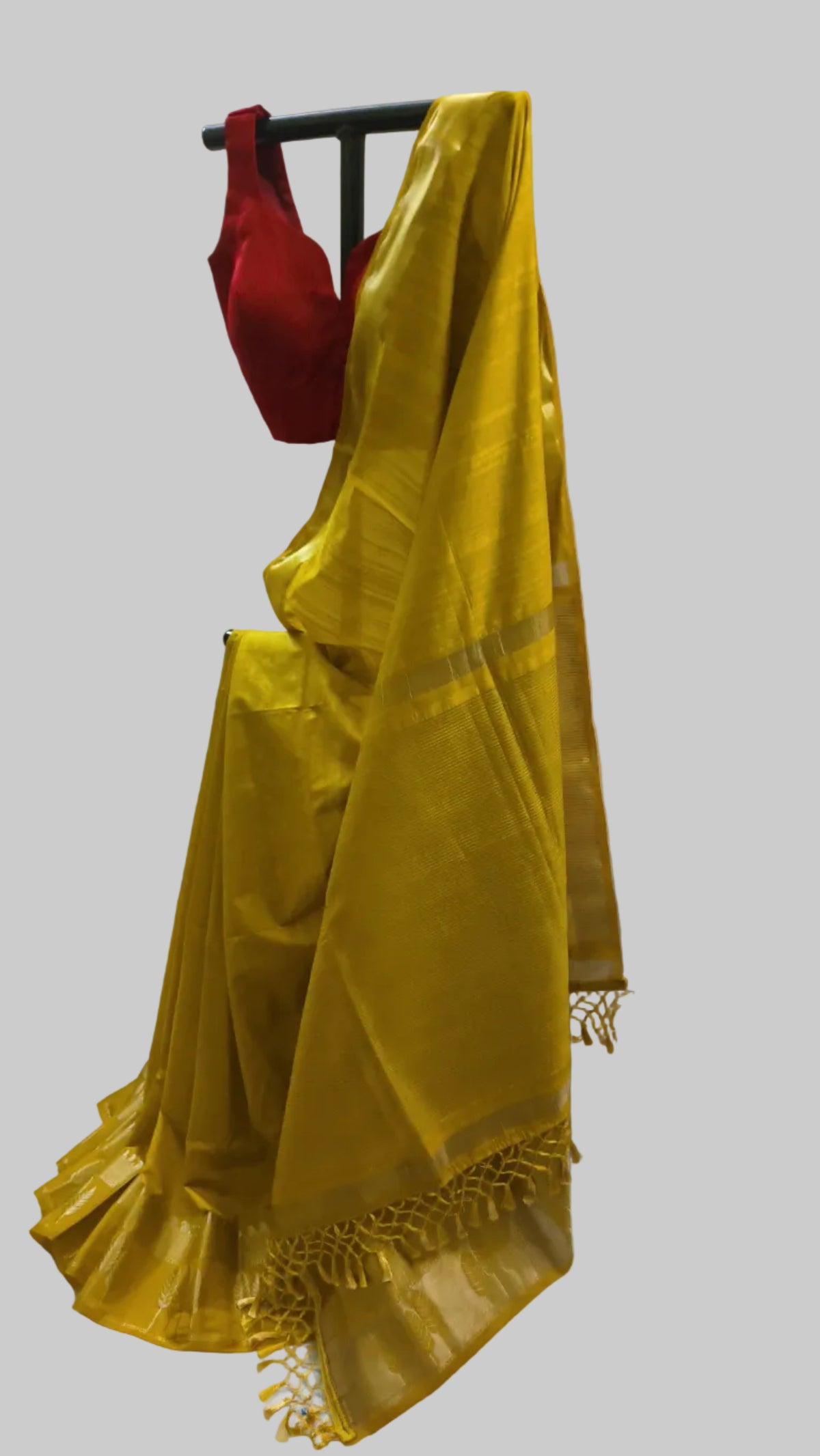 A yellow silk saree draped on a black hanger with a red blouse, set against a white fabric backdrop.
