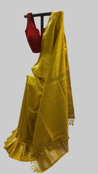 A yellow silk saree draped on a black hanger with a red blouse, set against a white fabric backdrop.