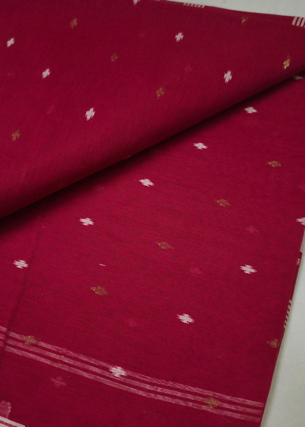 A folded and draped deep red fabric, likely a saree, featuring small scattered metallic gold and white motifs and a patterned border.