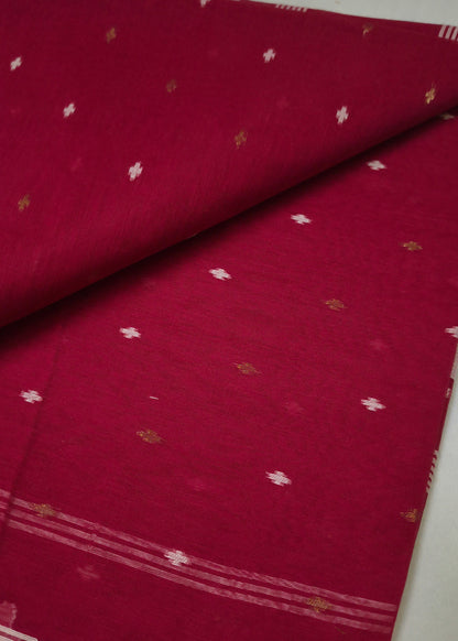 A folded and draped deep red fabric, likely a saree, featuring small scattered metallic gold and white motifs and a patterned border.