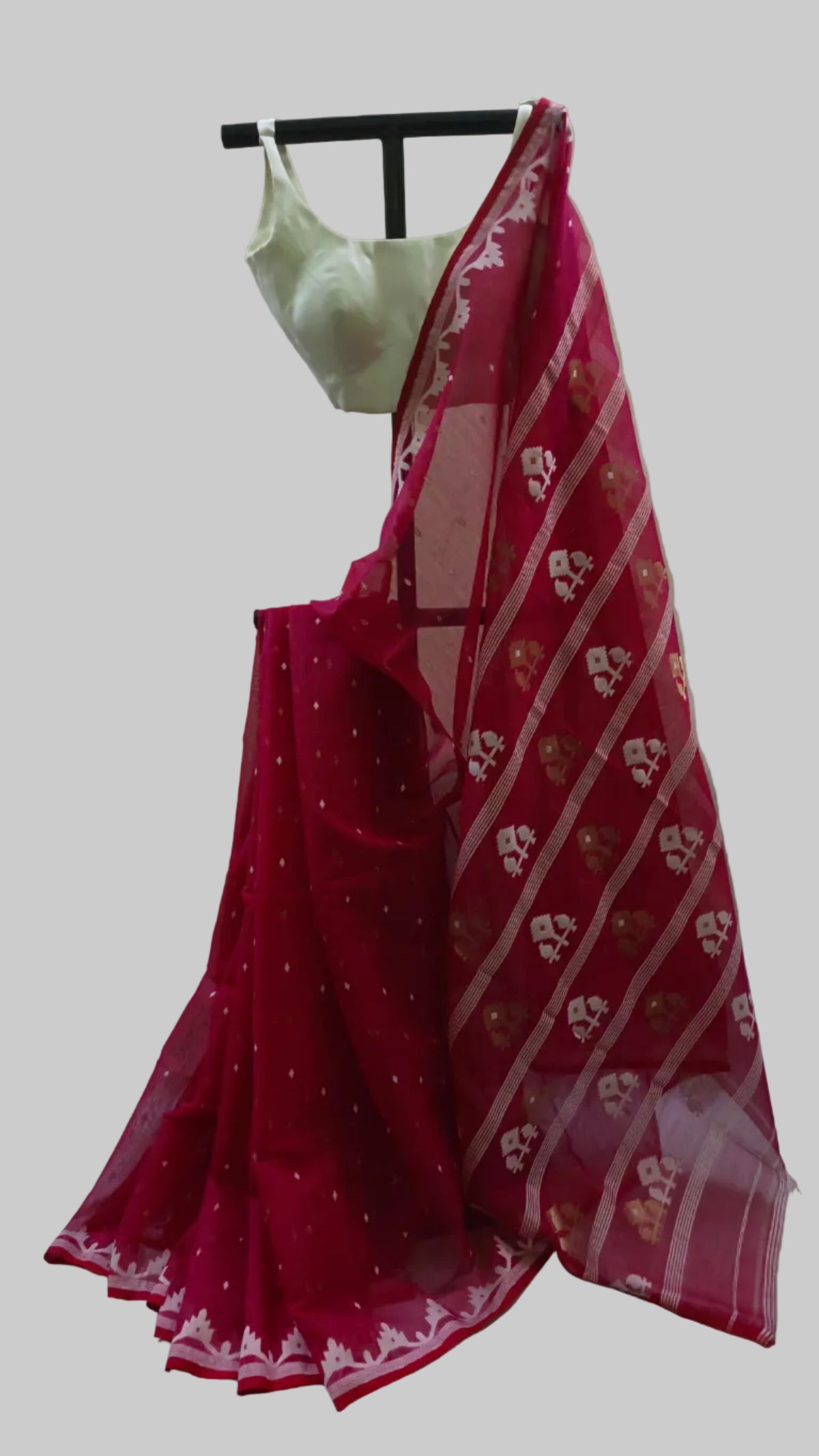 A deep pink georgette saree with white floral patterns and gold zari borders, paired with a white blouse, displayed on a black hanger against a draped beige fabric backdrop.
