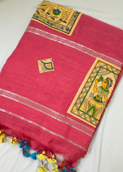 A folded pink saree or fabric piece with gold zari stripes, traditional hand-painted motifs in yellow, green, and blue, and colorful tassels along the edge, laid flat on a white surface.