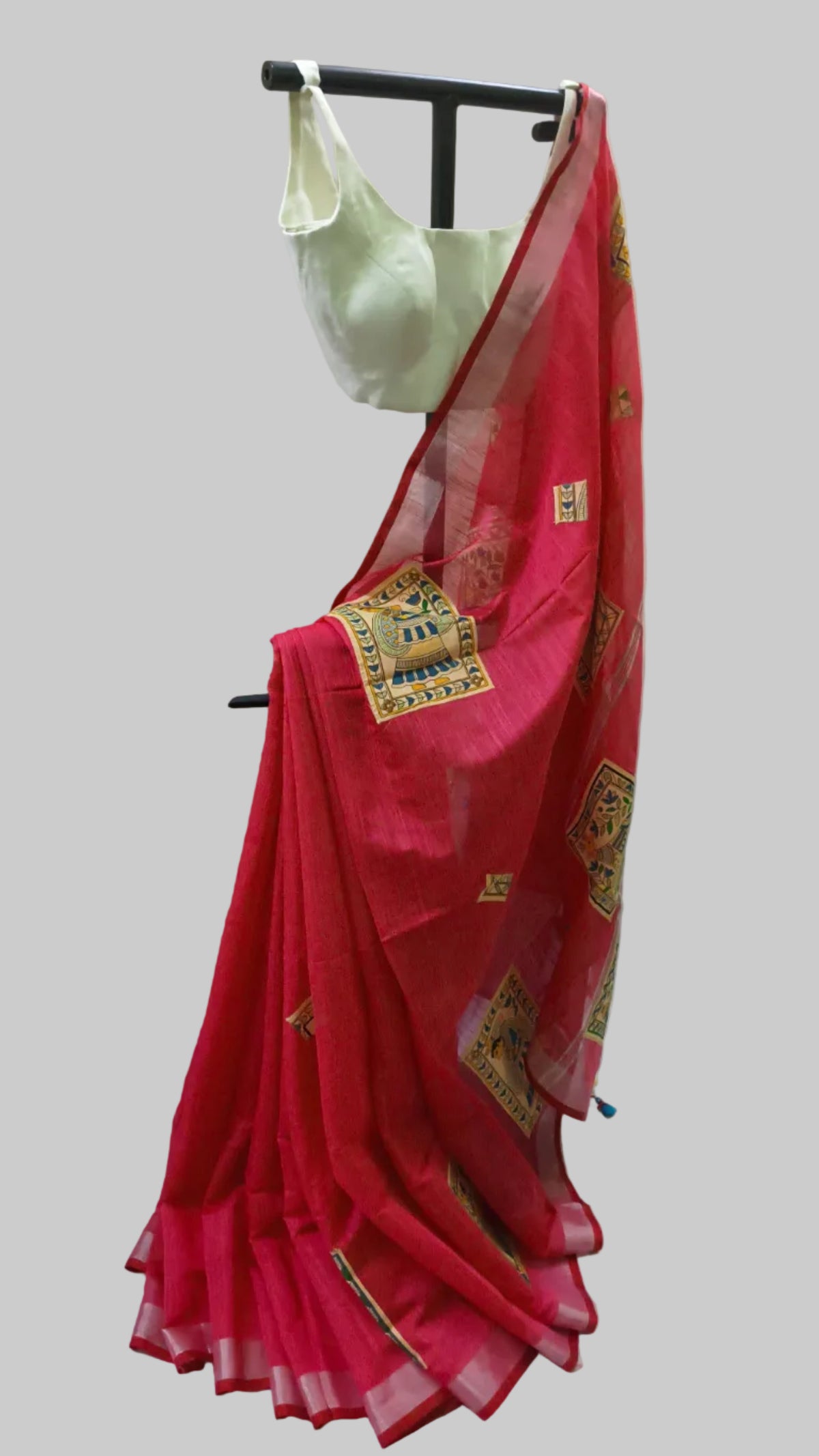 A pink silk saree with gold and green border patterns, draped on a black clothing stand alongside a light green blouse, set against a white fabric backdrop.