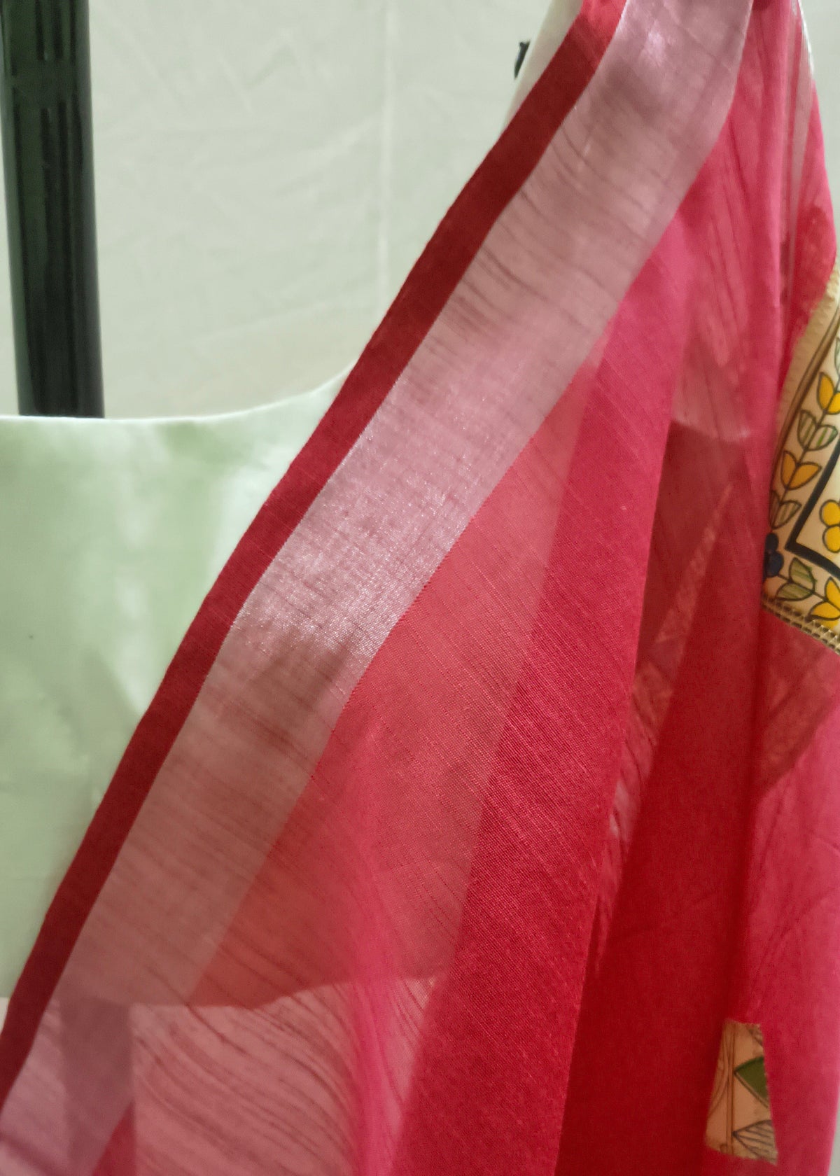 A close-up of a pink and red sheer dupatta draped over a white blouse, showing a patterned border with yellow, green, and red details.