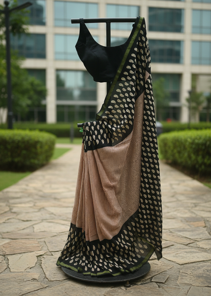 A black and beige saree with a black blouse is displayed on a black dress form stand outdoors on a stone pathway with a modern glass building in the background.