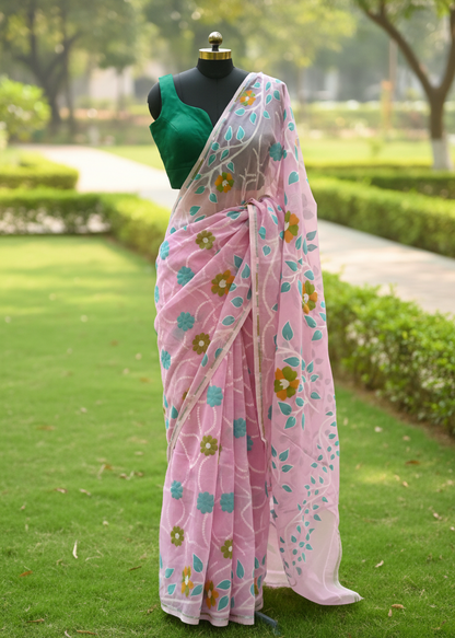 A pink floral saree draped on a black dress form mannequin, paired with a green sleeveless blouse, set against a blurred green garden background.