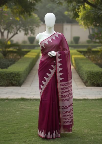 A deep magenta saree with cream geometric patterns and borders, displayed on a white mannequin in an outdoor garden setting.