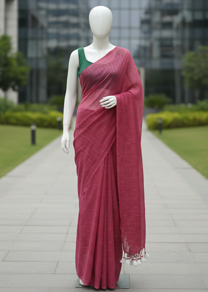 A mannequin wearing a draped pink saree with a green sleeveless blouse, standing on a paved walkway in front of a modern glass building.