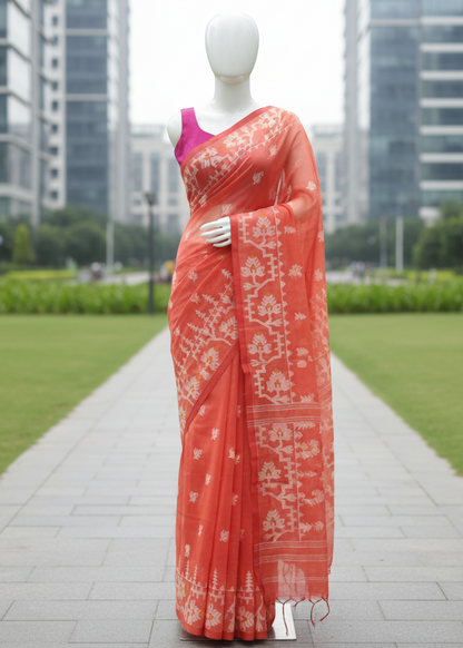 A coral orange saree with white floral patterns and a bright pink blouse displayed on a white mannequin outdoors on a paved path with green grass and modern buildings in the background.